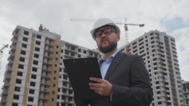 Sakallı bina müfettişi. Kasketli ve takım elbiseli. Not alıyor ve kendi kendine konuşuyor. Düşük açılı adam inşaat alanını inceliyor. Kontrol kavramı