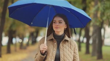 Parkta şemsiyesiyle gezen güzel, mutlu bir genç kadın. Arka planda bulanık ağaçlar. Boş zaman kavramı.