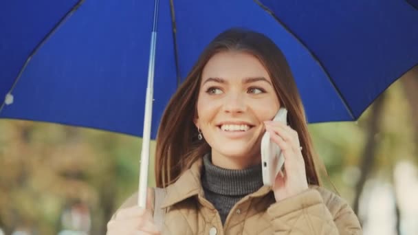 Fröhliche Junge Frau Telefoniert Während Sie Unter Ihrem Blauen Regenschirm — Stockvideo