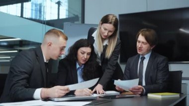 Ofiste toplanırken kağıtlara yazı yazan kadın liderli bir takım yöneticiler, yeni proje hakkında fikir alışverişinde bulunan ve görüşlerini paylaşan meslektaşlar, strateji planlayanlar. Takım çalışması kavramı