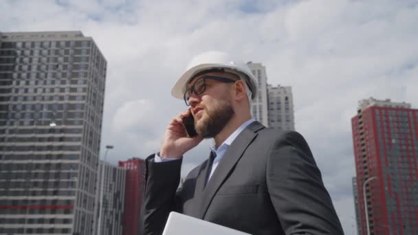 Hombre Con Casco Chaqueta Traje Caminando Con Portátil Contra Edificios — Vídeos de Stock