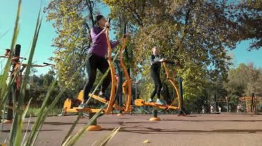 Spor giyimli atletik kızlar güneşli bir sonbahar gününde spor sahasında spor bisikletleriyle antrenman yapıyorlar. Şehir parkında kardiyo antrenmanı yapan neşeli arkadaşlar. Zindelik kavramı