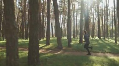 Siyah spor giysili formalı, parkta koşan spor ayakkabılı, ağaçların arasından parlayan bir adam. Atış yapan erkek koşucu dışarıda egzersiz yapıyor. Zindelik kavramı