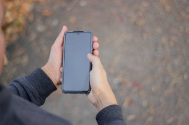 Yakından bakınca, erkek eli boş ekranlı akıllı telefon tutuyor. Model mesaj ya da içerik için hazır. Cep telefonlu bir adamın elleri. Boş ekran.