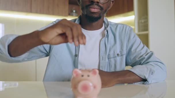 幸せなアフリカ系アメリカ人の男は貯金箱にお金を入れて将来のための資金を節約 — ストック動画