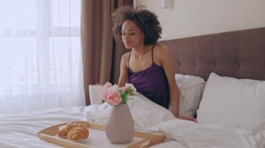 Mutlu siyah kadın yatakta sabah kahvesini içiyor, otelde dinleniyor, tatilde.