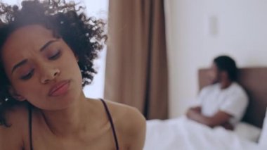 Mutsuz genç bir kadın yatakta oturuyor, gücenmiş kocaya bakıyor, evlilik krizi geçiriyor.