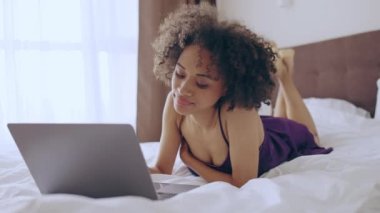 Güzel bir kadın dizüstü bilgisayarla yatakta yatıyor, çöpçatanlık sitesine bakıyor, alışveriş yapıyor.