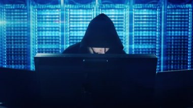 Bilgisayar korsanı klavyede yazıyor, sunucu odasında monitörlerin arkasında oturuyor. Hackerların geçmişe dönük komik tasviri