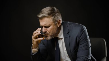 Zarif takım elbiseli üzgün sakallı adam sert viski içiyor, yalnız oturuyor.
