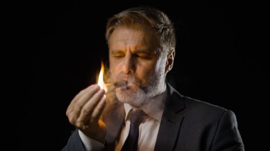 Başarılı bir iş adamı puro içiyor, karanlık odada oturuyor, zaferi kutluyor.