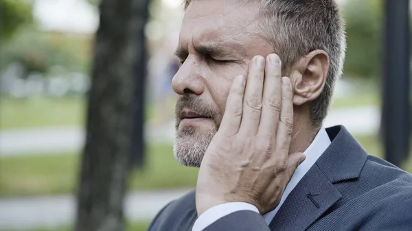 Middle-aged man suffering from headache or panic attack, breathing fresh air outdoor