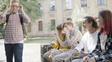 Okullu çocuklar gözlüklü tombul sınıf arkadaşlarına gülüyorlar. Kilo kabadayılığı.