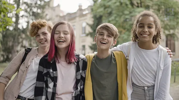 Heyecanlı çok ırklı okul çocukları kameralara sarılıp gülümsüyor.