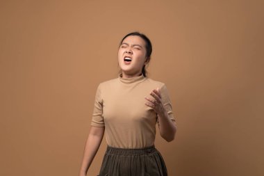 Asyalı kadın boğazı ağrıyordu, öksürüyordu, hapşırıyordu ve bej arka planda tek başına duruyordu..