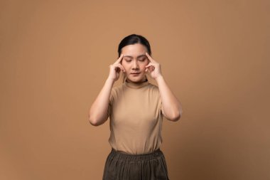 Asyalı kadın hastaydı. Başı ağrıyordu. Bej arka planda tek başına duruyordu..