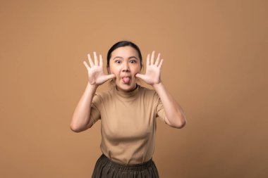 Asyalı neşeli bir kadın, bej arka planda tek başına dikilip ellerini göstererek bir böceği dikizliyor..