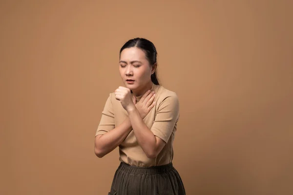 アジアの女性は喉が痛くて咳がしてくしゃみをしてベージュ色の背景に孤立して立っていた — ストック写真