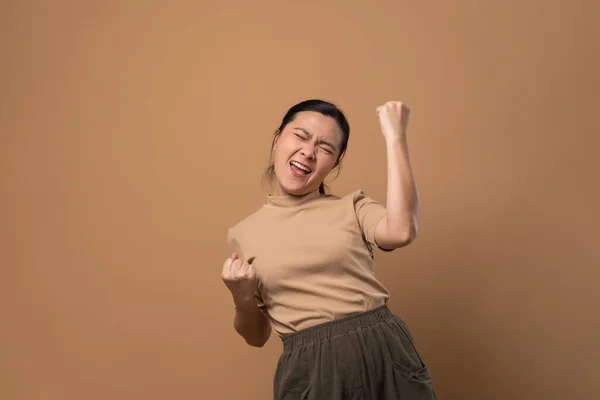 アジアの女性幸せな自信立って見せます彼女の拳作りA勝利ジェスチャー隔離された上ベージュ背景 — ストック写真