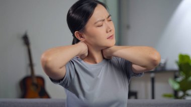 Asian woman was sick with body pain touching her body sitting on sofa in living room at home.