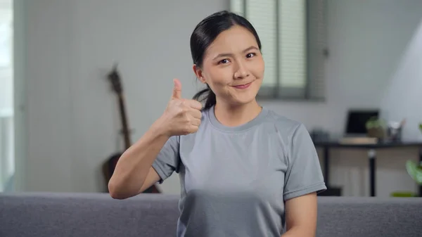微笑着自信的亚洲女人看着相机 然后在家里客厅的沙发上竖起大拇指 — 图库照片