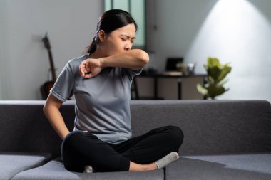 Asyalı kadın ateşlenmişti öksürüyordu ve evdeki oturma odasında kanepede rahatsız hissediyordu..