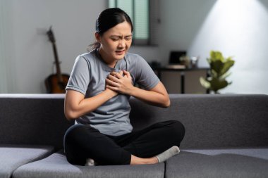 Göğsüne dokunan Asyalı kadın, oturma odasındaki kanepede oturup göğsü ağrıdığı için hastaydı..