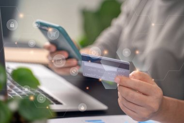 Close up shot of females hands holding credit card typing message on smart phone with technology icons for shopping online at home office.