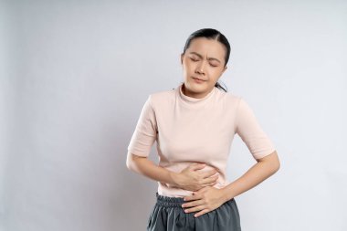 Asian woman was sick with stomach ache, putting her hands on her belly and standing isolated on white background.