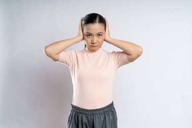 Asyalı kadın sıkılmış ve sinirlenmiş, kulaklarını kapatmış, beyaz arka planda soyutlanmış..