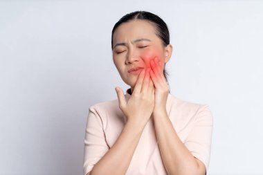 Asian woman was sick with toothache touching her cheek with red point and standing isolated on white background.