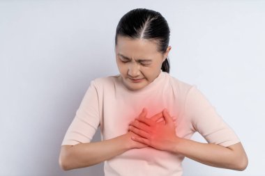 Asian woman having chest pain holding hands on chest with red spot, standing isolated on white background.