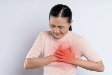 Asian woman having chest pain holding hands on chest with red spot, standing isolated on white background.