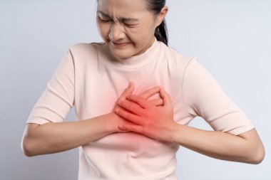 Asian woman having chest pain holding hands on chest with red spot, standing isolated on white background.