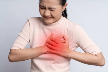 Asian woman having chest pain holding hands on chest with red spot, standing isolated on white background.