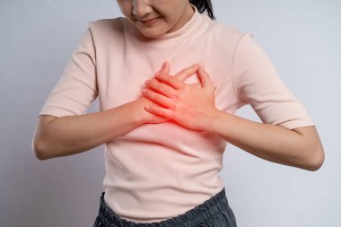 Asian woman having chest pain holding hands on chest with red spot, standing isolated on white background.