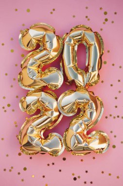 Mutlu yıllar 2022 kutlamaları. Parlak altın balon figürleri, pembe arka planda parıldayan yıldızlı yeni yıl balonları. Noel kutlaması. Hediye kartı.