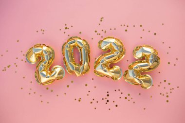 Mutlu yıllar 2022 kutlamaları. Parlak altın balon figürleri, pembe arka planda parıldayan yıldızlı yeni yıl balonları. Noel kutlaması. Hediye kartı.