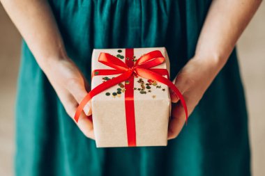 Kırmızı kurdeleli mutlu noel hediyesini tutan kadın, yeni yıl sürprizini hazırla neşeli el yapımı Noel hediyesi.