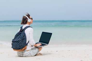 Güzel bir tropik plajda otururken dizüstü bilgisayarda klavye kullanan ve daktilo kullanan bir kadın. Serbest çalışma, tatiller, mesafe çalışması, sosyal uzaklık, e-öğrenme, bağlantı, yaratıcı meslek, yeni iş, online konsept buluşması