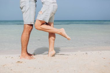 Bacakları sahilde. Ayak spası. Kumsalda sarılıp öpüşen genç bir çift. İki sevgili, erkek ve kadın, okyanus kenarında yalınayak. Yaz aşkı.