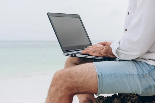 男子在海滩上蓝色的大海前的笔记本电脑上打字 概念远程工作 自由职业 — 图库照片