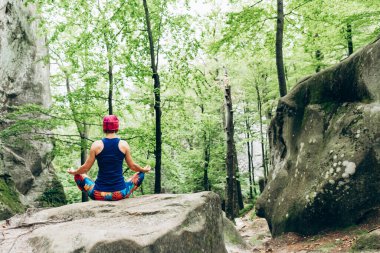 Ormanın içinde bir kaya üzerinde yoga yaparken meditasyon lotus poz, kadın