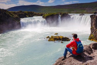 Kırmızı ceketli adam Godafoss şelalesine bakıyor. İzlanda 'nın güzel manzarası