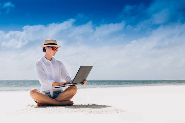 женщина использует и печатает на ноутбуке, сидя на пляже