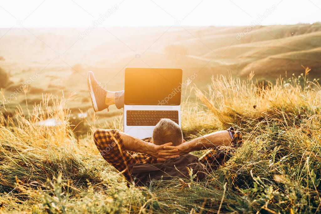 Man working outdoors with laptop sitting in mountains. Concept of remote work or freelancer lifestyle. Cellular network broadband coverage. internet 5G. Hiker tourist enjoying valley view sunset