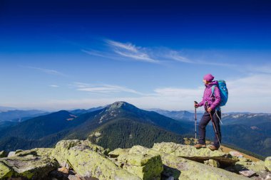 Sırt çantalı kadın gezgin dağlarda yürüyüş yapıyor. Arka planda güzel bir yaz manzarası var. Spor yaşam tarzı kavramı.