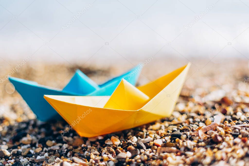 Blue and yellow paper boats on the pebble beach