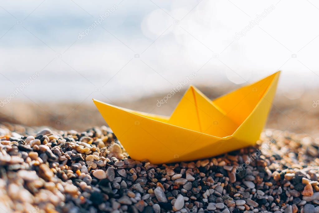 Yellow paper boat on the pebble beach