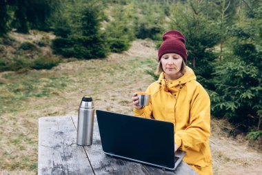 Dışarıda dizüstü bilgisayarda çalışan güzel doğayla çevrili bir kadın.